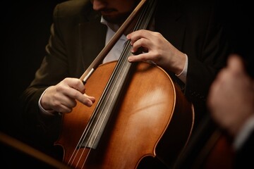 Close up on hand of unrecognizable devoted male musician strumming cello while playing with chamber quartet in dramatic light, focus on fingers and strings