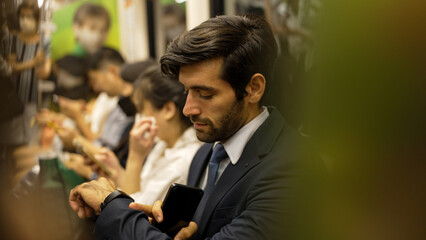 Smiling caucasian business man looking at mobile phone or playing social media while sitting in train. Attractive project manager going to work place by using public transport in rush hour. Exultant.