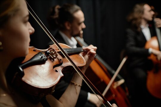 Cropped side view shot of unrecognizable female musician playing violin with chamber quartet on stage, focus on string instrument and bow