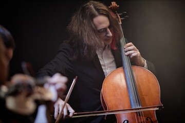 Passionate male cellist playing classical music with string quartet in dark hazy studio © Seventyfour