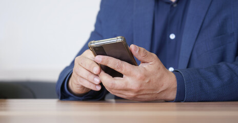 Man in a business suit uses a mobile phone in a transparent silicone case. Manager, lawyer, businessman, politician, attorney or official. No face. Photo. Selective focus