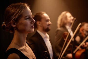 Side view portrait of dignified female violinist standing in row with string quartet receiving...