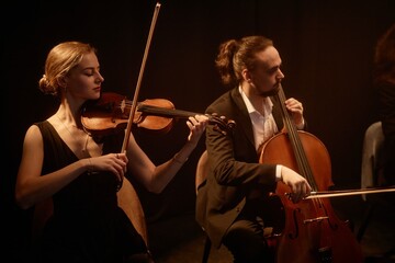 Side view of female and male classical music artists playing violin and cello in string quartet,...