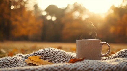 A cozy cup of steaming coffee on a knitted blanket, surrounded by autumn leaves in a tranquil sunset setting.