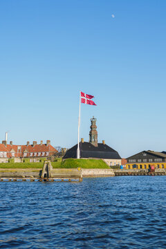 A Danish flag waves on a tall flagpole situated on grassy hill