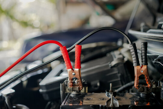 Close-up of car charger cable jump starting a dead car battery. Black and red charging cable clamps on battery terminals for charging, car repair and maintenance concept.