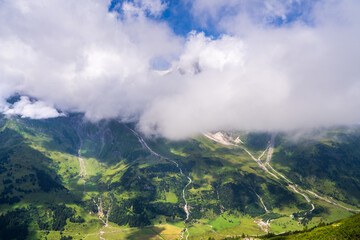 Majestic mountain peaks covered with clouds. Mountain rivers, waterfalls quickly flow down. The famous high mountain road Grossglocknerstrasse. Austria. Hohe Tauern Park.