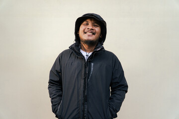 Portrait of Asian man wearing adventure clothes and doing various poses. Macho and smiling adult man wearing white shirt and jacket with hood isolated on beige background