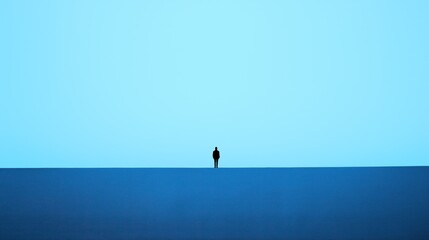 Fototapeta premium A lone person stands on a flat surface, gazing out at the vast blue horizon, with the atmosphere evoking feelings of tranquility and contemplation during dusk