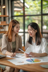 Obraz premium Dynamic Collaboration Between Two Asian Businesswomen Analyzing Data in a Modern Office Environment