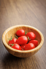 Red cherry tomatoes in bowl on wooden table.