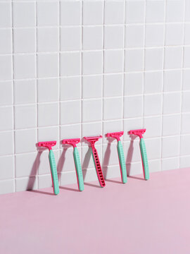 Five Pink Razors Aligned Against Tiled Wall in Minimalist Settin