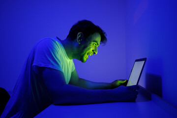 Man Engaged in Digital Interaction While Bathed in Blue and Green Light at Night