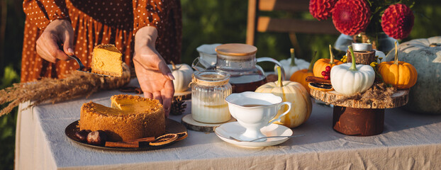 Elegant countryside table setting outdoor in the garden. White porcelain cups, teapot with herbal tea, homemade pumpkin spicy sweet pie. Family tradition, beautiful place outside. Fall mood. Banner