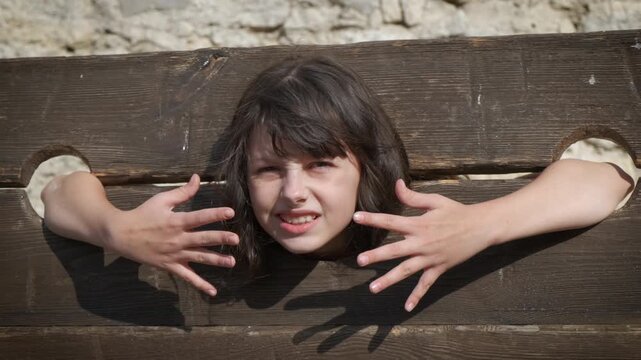 Child enjoy medieval festival. A view of little girl try to play with medieval guillotine in the sun light.