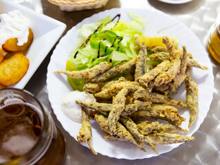 Portion of fried anchovies served with greens, lemon and white creamy sauce