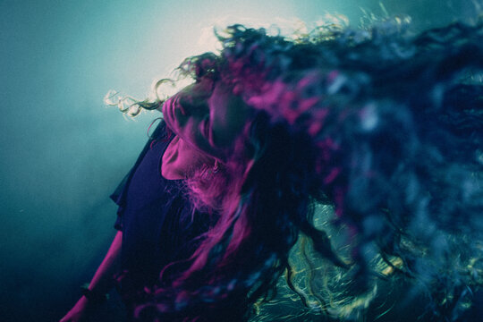 A young woman with curly hair flips her head back in a dynamic motion