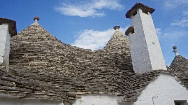 Traditional trullo house in alberobello, italy, showing characteristic stone roof and white chimney under a blue sky