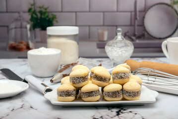 Homemade cornstarch alfajores with dulce de leche and grated coconut on a kitchen counter with the ingredients flour sugar coconut whisk
