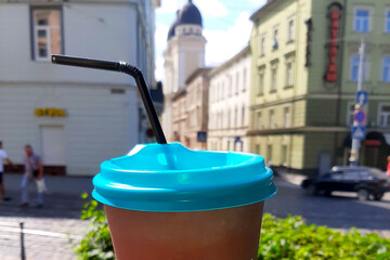 Naklejka premium Refreshing Coffee in a Brown Cup With Blue Lid Against a City Summer Backdrop