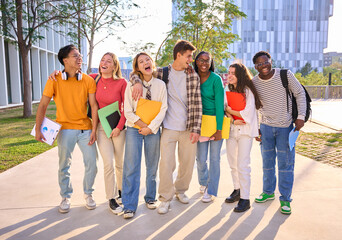 Group of generation z international university students laughing standing hugging together on campus garden. Young diverse people looking smiling at each other holding backpacks and workbooks outdoors