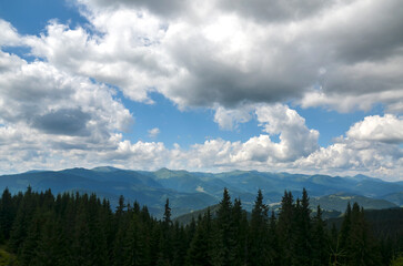 Scenic landscape featuring a vast expanse of rolling hills covered in dense green forests with mountain ridge on background under sky with low clouds. Carpathian Mountains, Ukraine