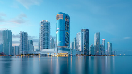 Obraz premium A contemporary waterfront city skyline with sleek, modern skyscrapers reflecting in the tranquil water at dusk. The sky is clear, enhancing the city's architectural beauty.