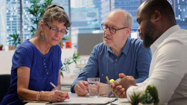 Middle aged couple exploring life insurance contract terms with financial adviser expert, reading pension option and planning an investment for retirement. Professional advice. Camera A.