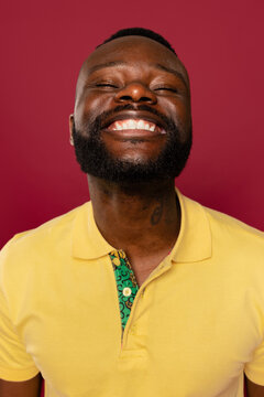 Man smiling brightly in yellow shirt against solid red background
