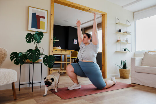 Curvy woman doing yoga at home with her dog