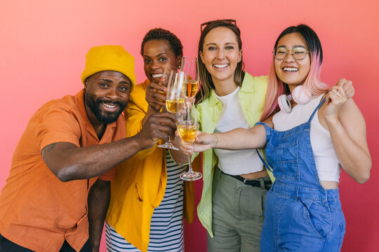Diverse friends toasting with champagne against a pink background.