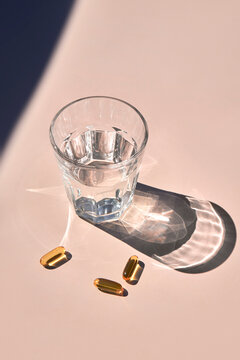 Omega 3 Capsules and Glass of Water under Sunlight on Beige Backdrop