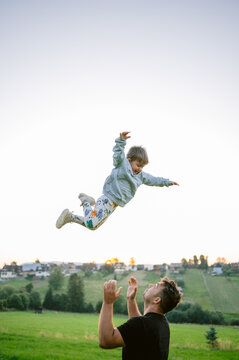 Father Tossing Son in Air During Sunset in Rural Field