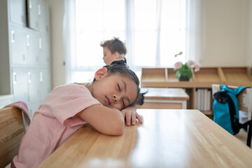Adorable young student sleeping on study table at elementary school.