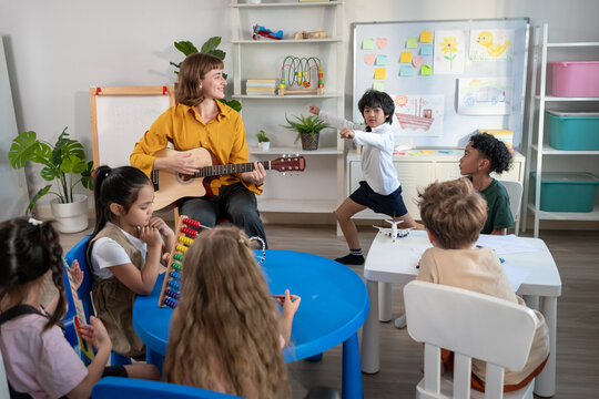 Caucasian young woman teacher playing guitar with student in school.