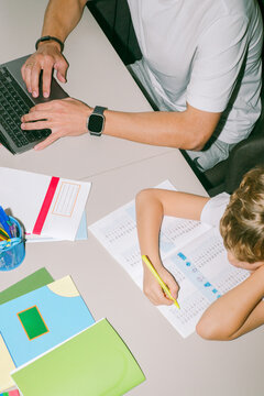 A son grudgingly does his homework next to his father 