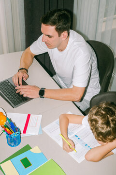 A son grudgingly does his homework next to his father 