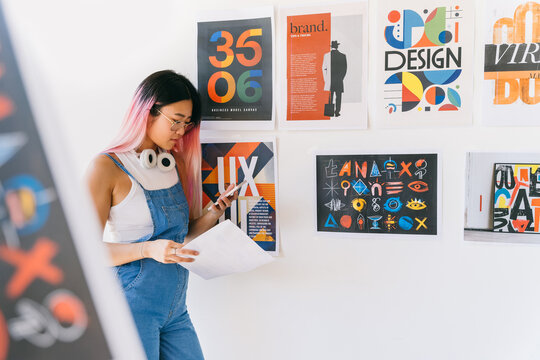 Chinese graphic designer reviewing work while standing besides posters