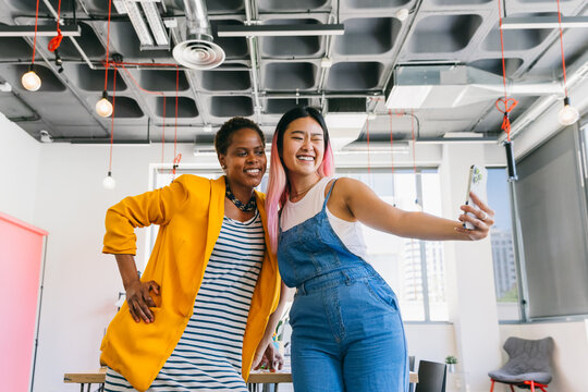 Friends taking a selfie in an office setting, expressing happiness