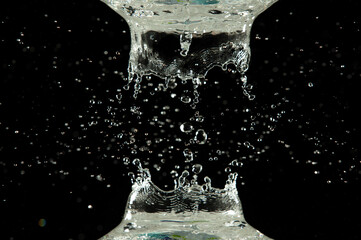 Crown water to object make curve drop explosion in ripple motion. Black background isolated. Crown Water splash on object to create shape form fluttering in droplet and wave.