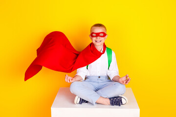 Photo of cheerful funny boy wear uniform red mantle sit enjoy yoga isolated on yellow color background