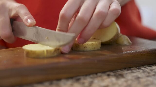 Mano cortando una papa sobre una tabla de madera. Mujer cocinando. Mano de mujer vestida de rojo cocinando. Cortar papa. Cocina saludable. Cocinar. Footage de Cocina.