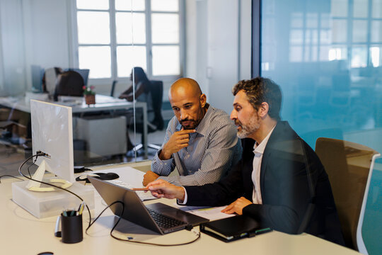 Two businessmen discussing work on laptop in modern office