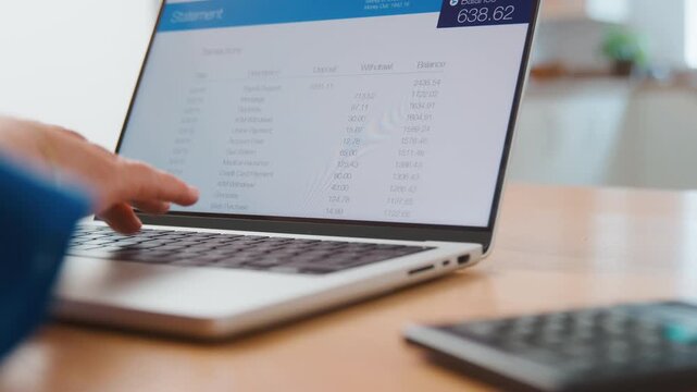 Person reviewing financial details on a laptop with calculator nearby.