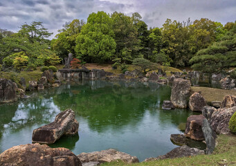 Carefully manicured Japanese landscape on a rainy day featuring pond in the foreoground and trees in the background