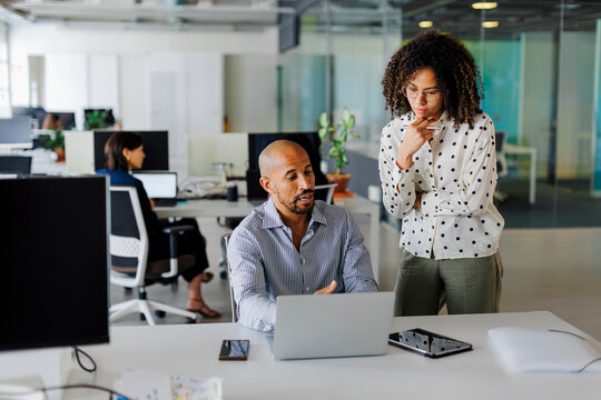 Business people discussing work at laptop in busy open plan office - Powered by Adobe
