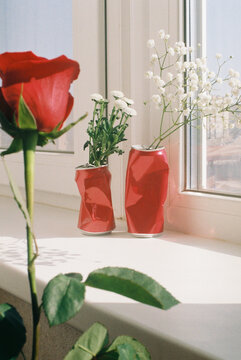 Dented red cans with flowers on a windowsill