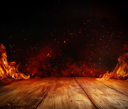 wooden table with Fire burning at the edge of the table, fire particles, sparks, and smoke in the air, with fire flames on a dark background to display products	and spicy foods