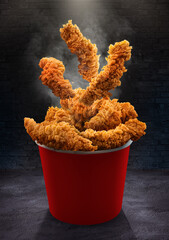 Fried chicken Hot crispy strips crunchy pieces of chicken breast tenders in a Bucket - a large Red box on the black table in the restaurant   © Mohamed