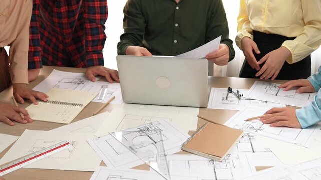 Smart architect and safety engineer discussion about building plan on table with architectural document, measurement tools and wooden block scatter around at modern office. Closeup. Delineation.